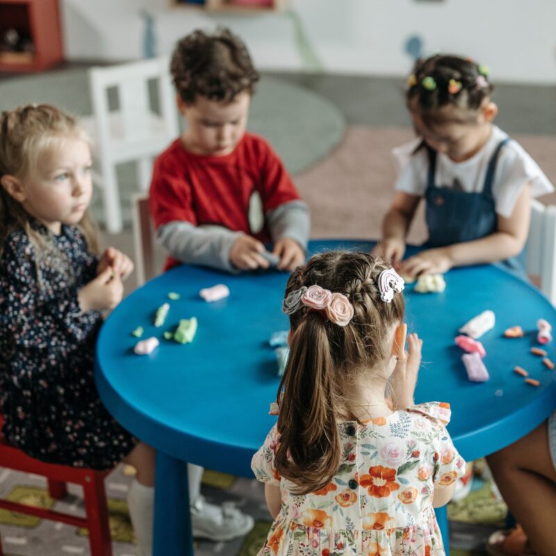 Cinq enfants autour d'un table qui font une activité bricolage.
