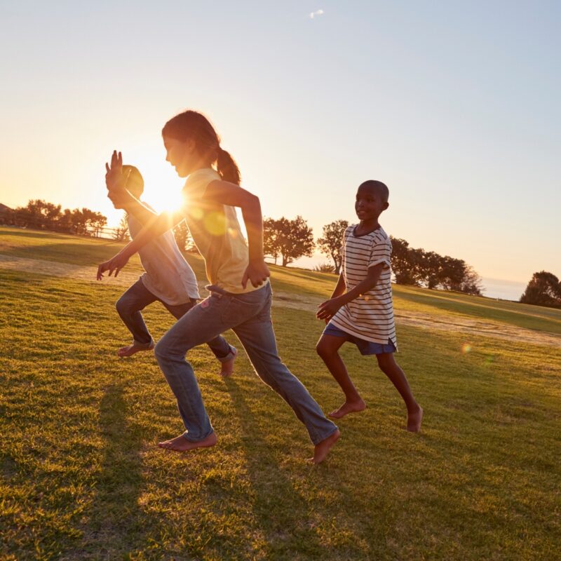 Trois enfants courent dans une prairie sous le soleil couchant.